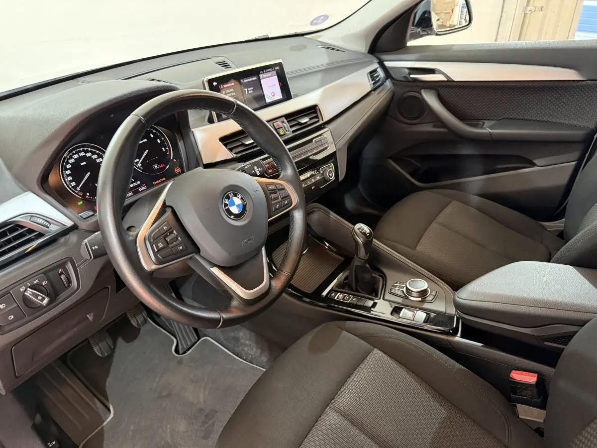 Vue intérieure côté conducteur de la BMW X2 sDrive18i Lounge 2023, tableau de bord et volant cuir multifonctions.