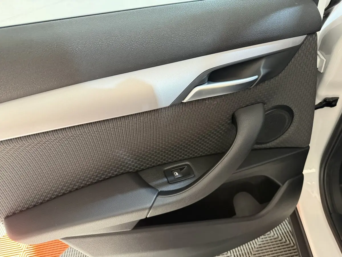 Détail de la porte intérieure côté conducteur d’une BMW X2 sDrive18i blanche, avec poignée noire et insert gris.