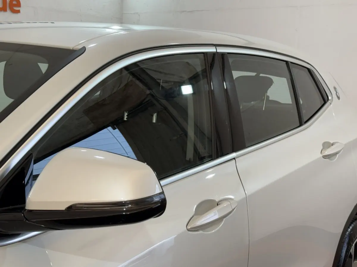 Vue latérale gauche rapprochée du BMW X2 sDrive18i Lounge blanc, mettant en valeur la poignée et le rétroviseur.