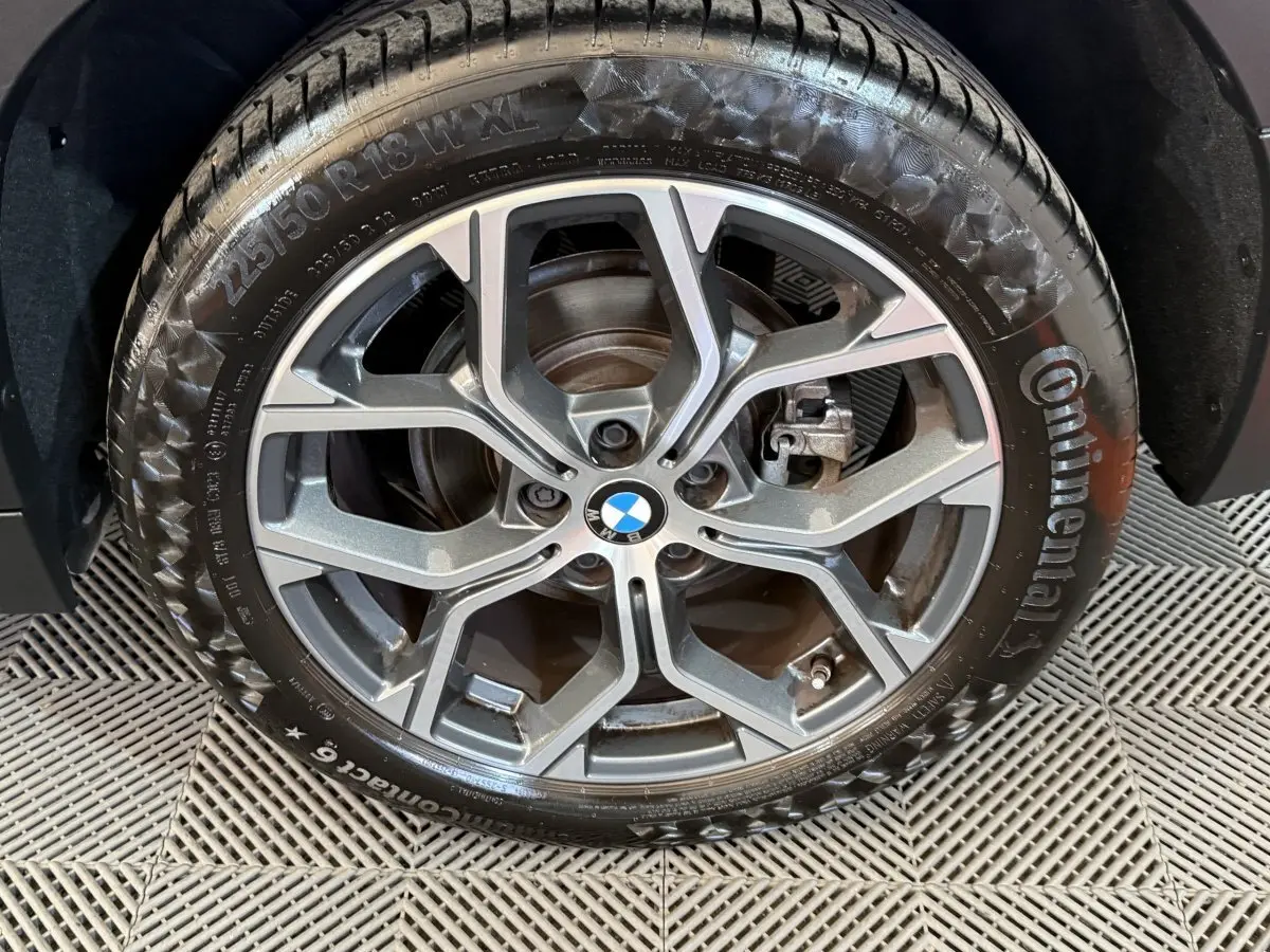 Gros plan sur la roue avant droite d’une BMW X2 blanche 2023, avec jante alliage à design moderne et logo BMW central.