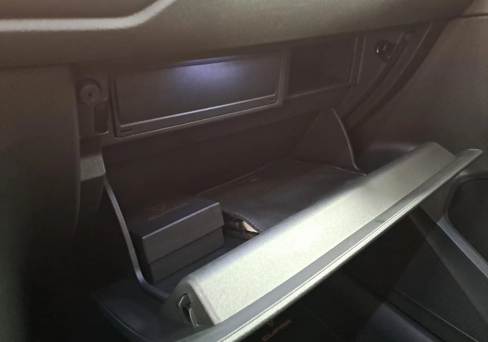 Gros plan sur la boîte à gants ouverte du CUPRA Ateca 2024, avec accessoires noirs à l’intérieur, vue côté passager.