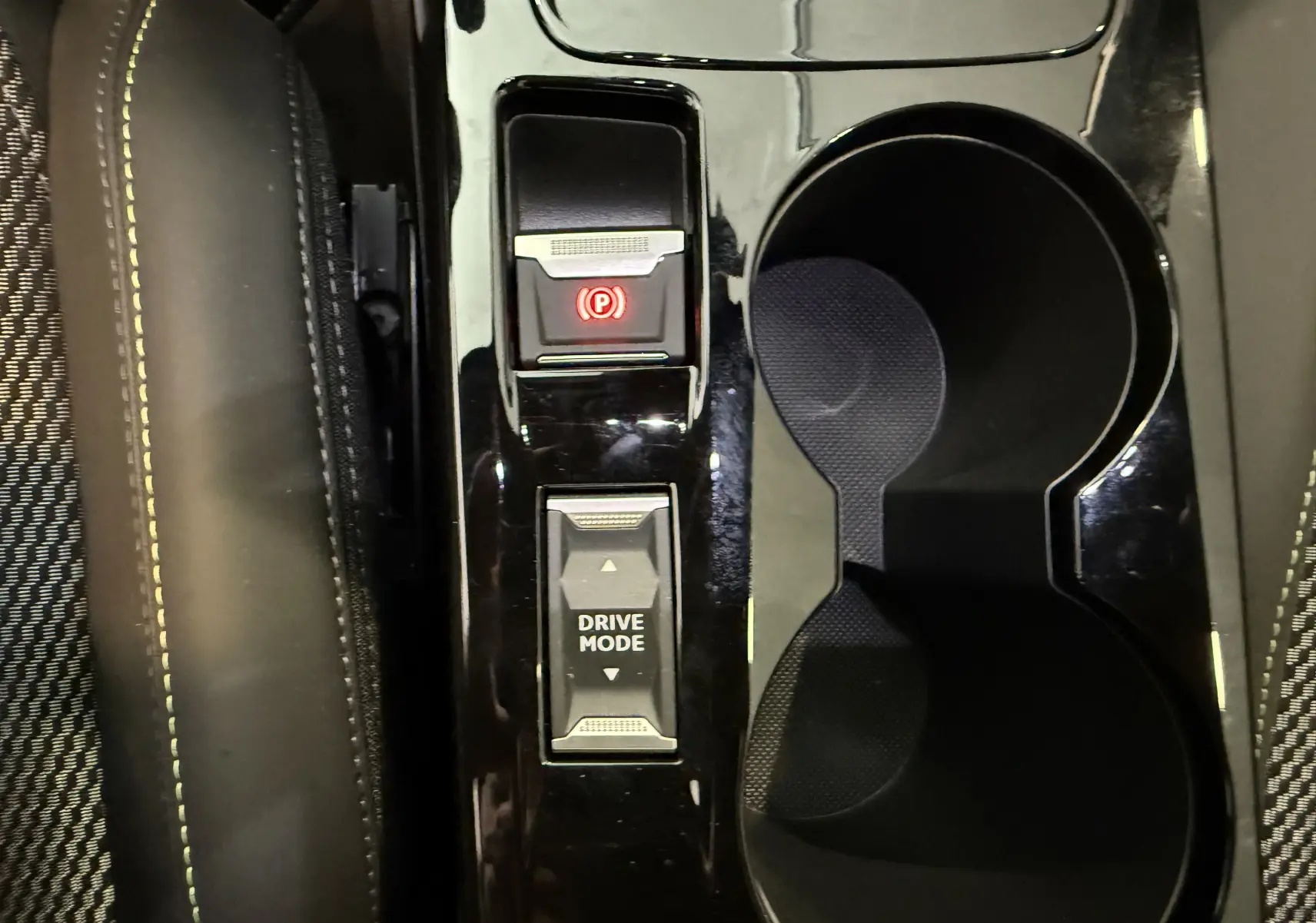 Gros plan sur la console centrale noire brillante du Peugeot 2008 2025 avec bouton frein à main électronique et sélecteur mode conduite.