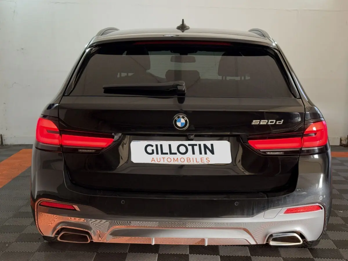 Vue arrière d'une BMW Série 5 Touring 520d noire avec feux LED allumés et double sortie d'échappement chromée.