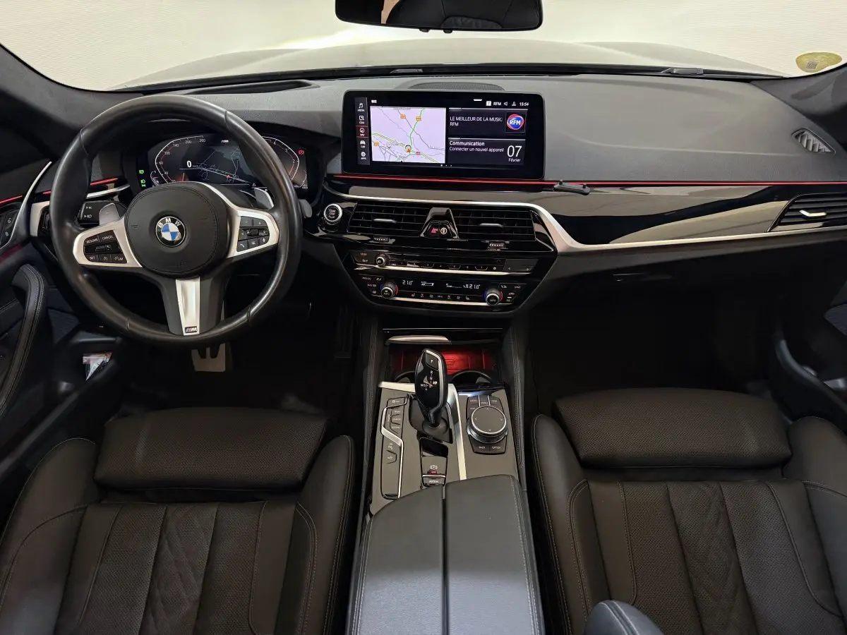Vue intérieure avant de la BMW Série 5 Touring 520d M Sport 2023, tableau de bord noir avec écran tactile et volant cuir alu.
