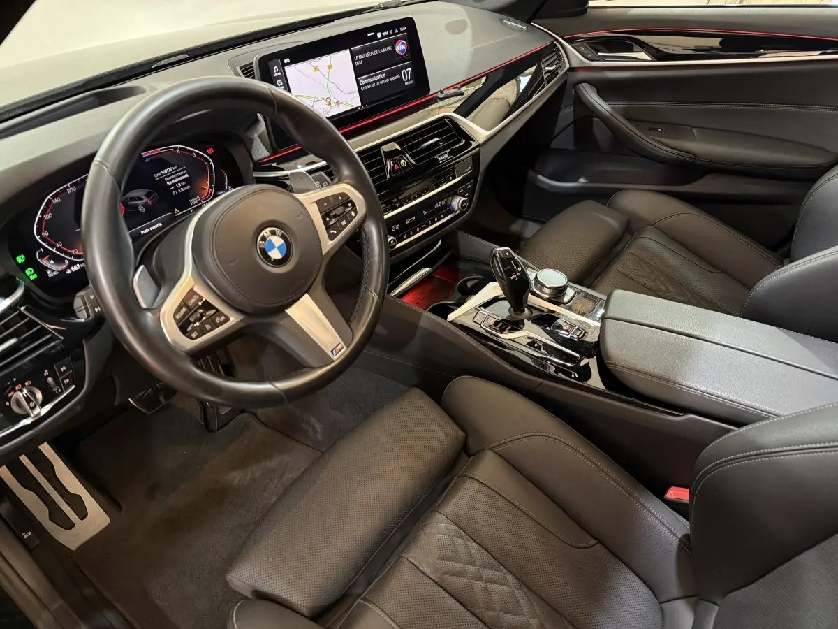 Vue intérieure côté conducteur de la BMW Série 5 Touring 520d M Sport 2023 avec tableau de bord digital et cuir noir.