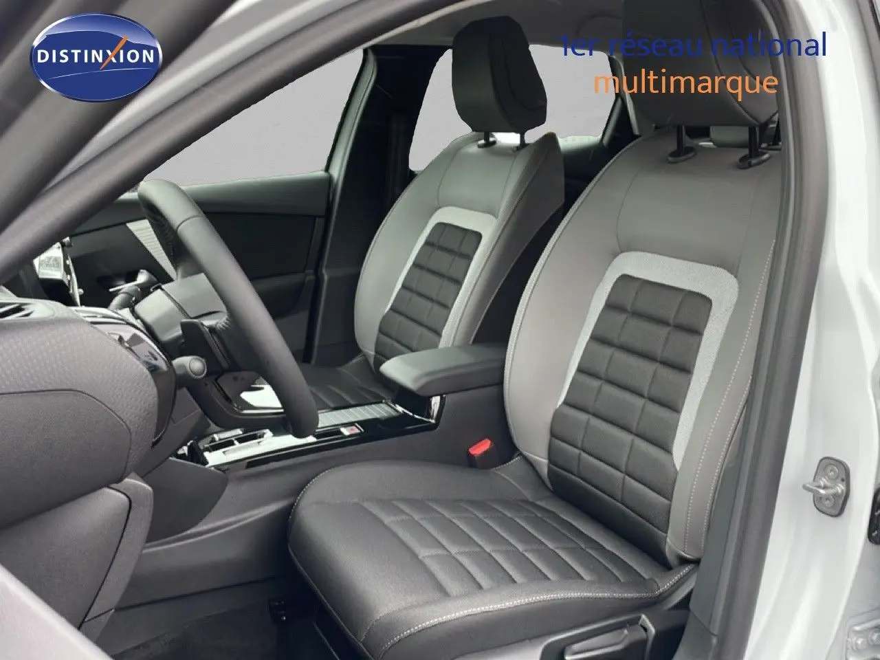 Vue intérieure côté conducteur de la Citroën C4 blanc métal 2026, sièges bi-matière gris et noir avec surpiqûres.