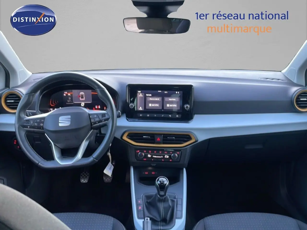 Vue intérieure frontale du tableau de bord du SEAT Arona blanc avec toit gris, volant cuir et écran tactile central.