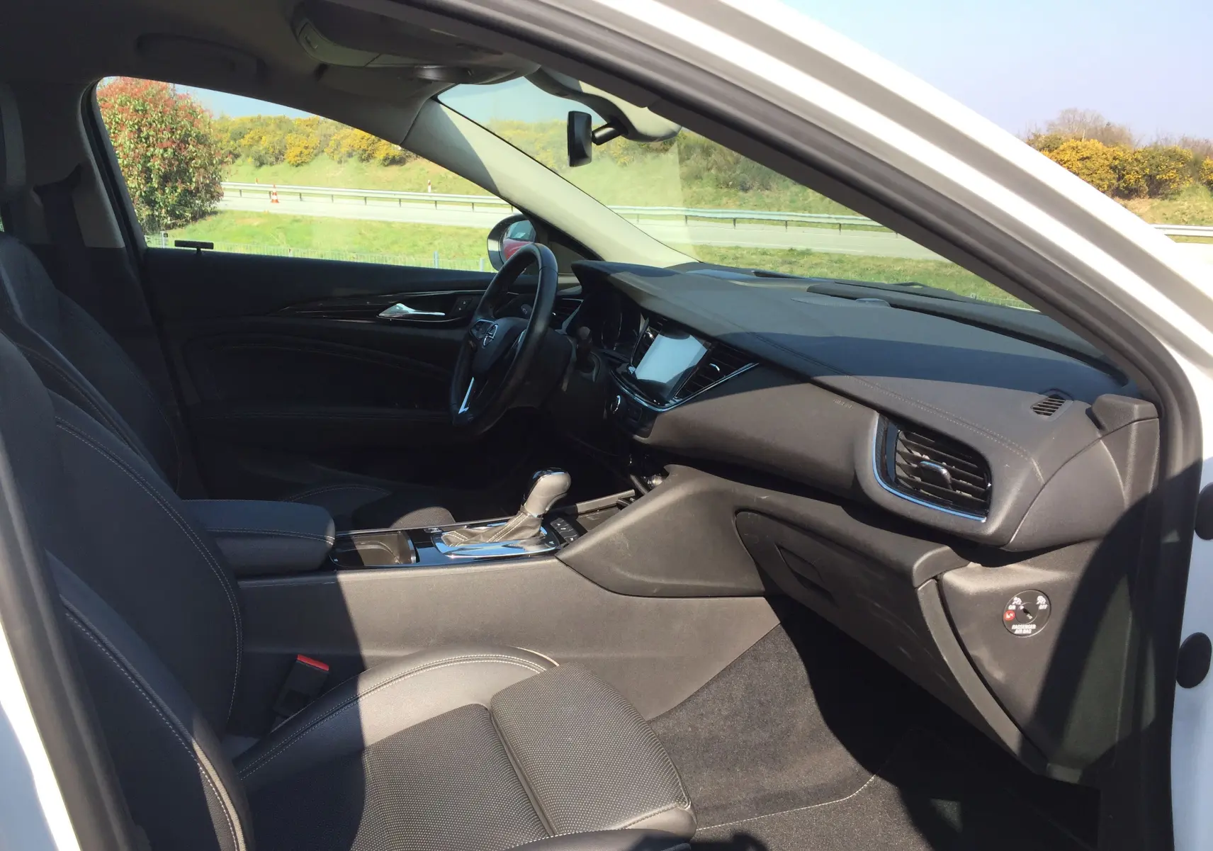 Intérieur noir de l'Opel Insignia Grand Sport blanc nacré, vue côté passager avec tableau de bord et console centrale visibles.