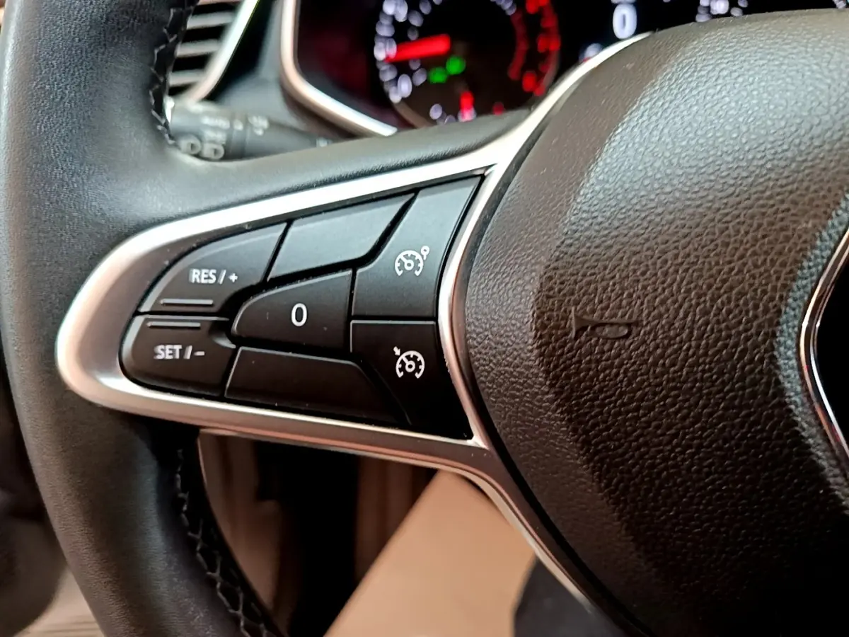 Gros plan sur les commandes du régulateur de vitesse au volant cuir noir de la Renault Clio Business blanche de 2021.