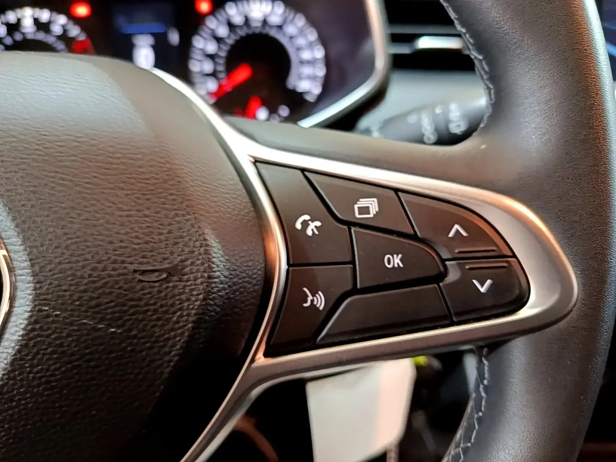 Gros plan sur les commandes multifonctions noires et argentées du volant cuir de la Renault Clio Business blanche, avec tableau de bord flou en arrière-plan.