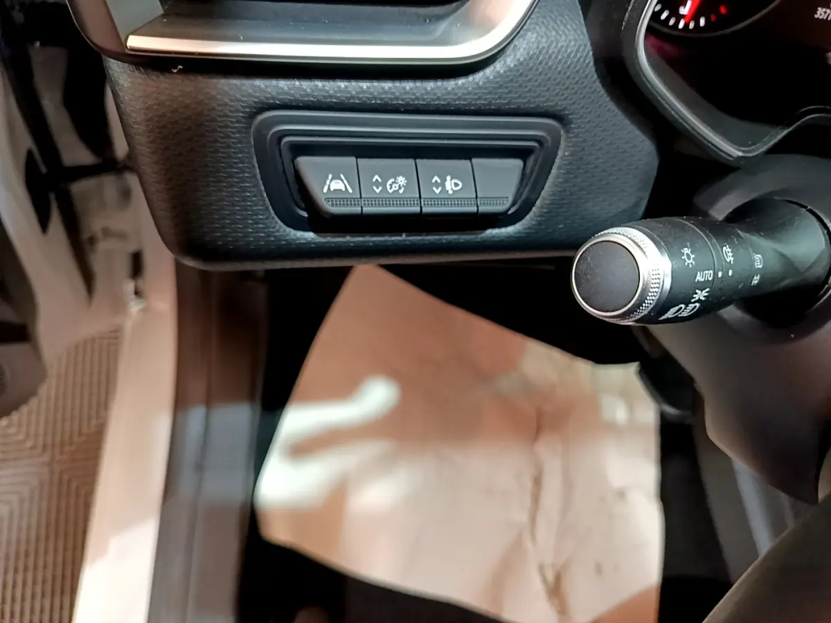Vue rapprochée de la commande des aides à la conduite et du commodo d’éclairage dans une Renault Clio Business blanche.