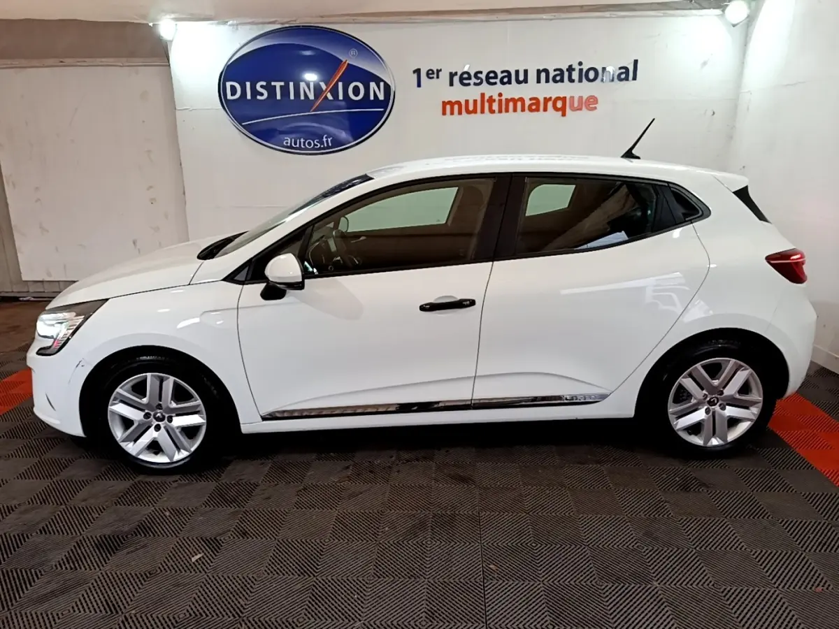 Profil droit d'une Renault Clio Business blanche 2021, avec jantes alliage et vitres teintées, en intérieur showroom.
