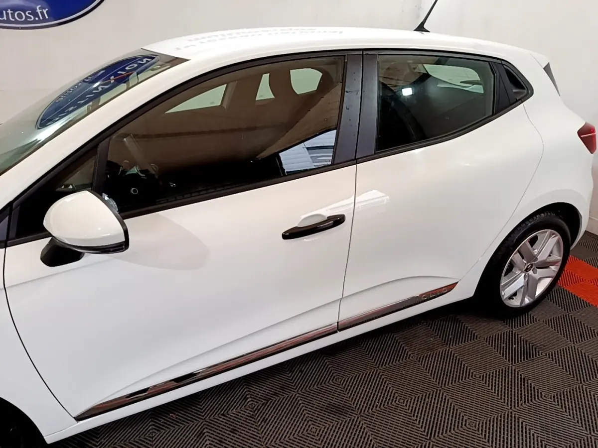 Profil droit d'une Renault Clio Business blanche, avec poignées et rétroviseur noir, sur sol à damiers noir et rouge.