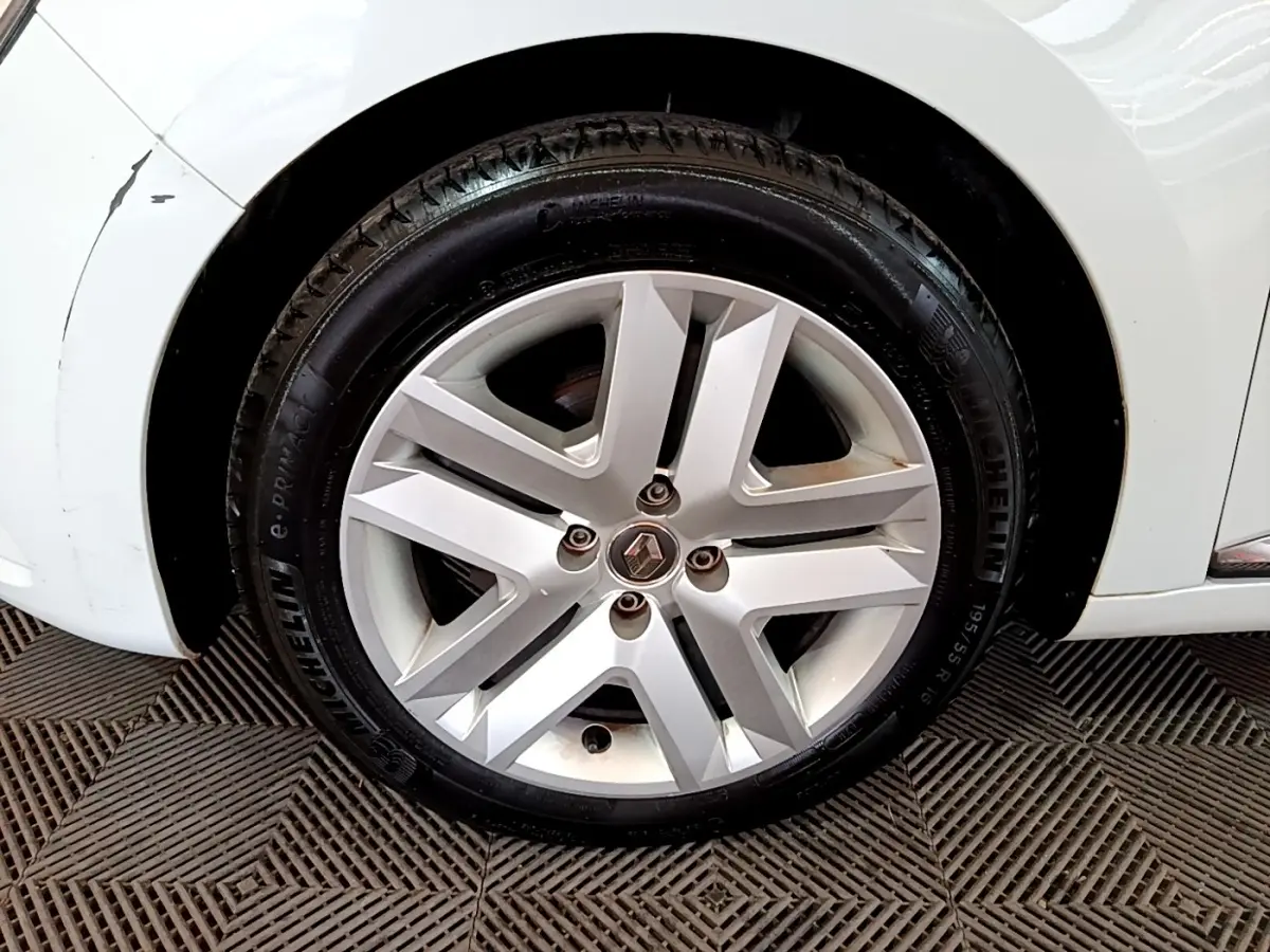 Gros plan sur la roue avant droite d'une Renault Clio blanche, jante alliage argentée au design moderne.