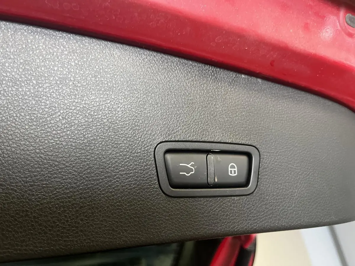 Gros plan sur le panneau intérieur rouge du coffre avec boutons d’ouverture et de verrouillage sur Alfa Romeo Tonale rouge.