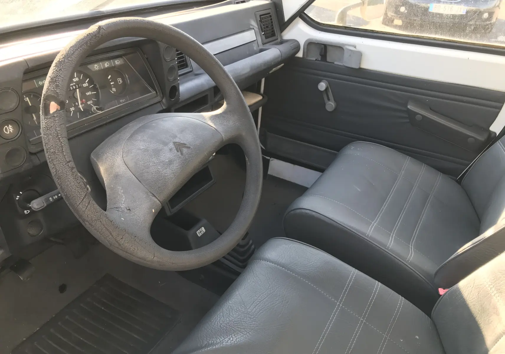 Intérieur du Citroën C15 Isotherm 1997 en vue côté conducteur, volant usé et sièges gris simples.