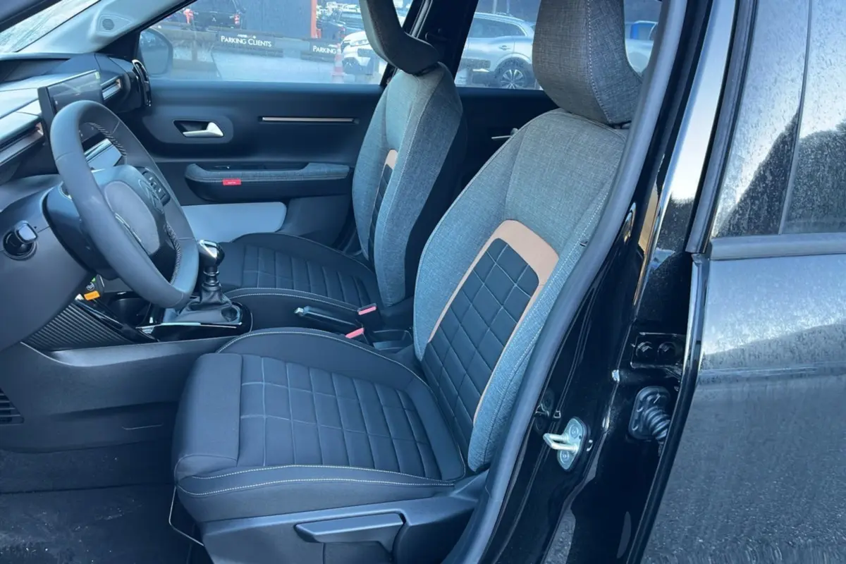 Vue intérieure côté conducteur de la Citroën C3 Aircross 2025 noire, sièges tissu bicolores avec volant cuir multifonctions.