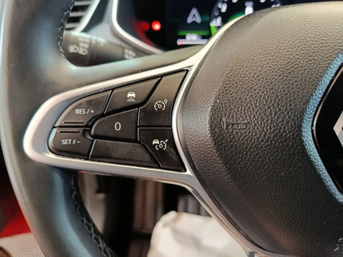 Gros plan sur les commandes de régulateur de vitesse à gauche du volant de la Renault Clio Techno TCe 90 rouge 2024.