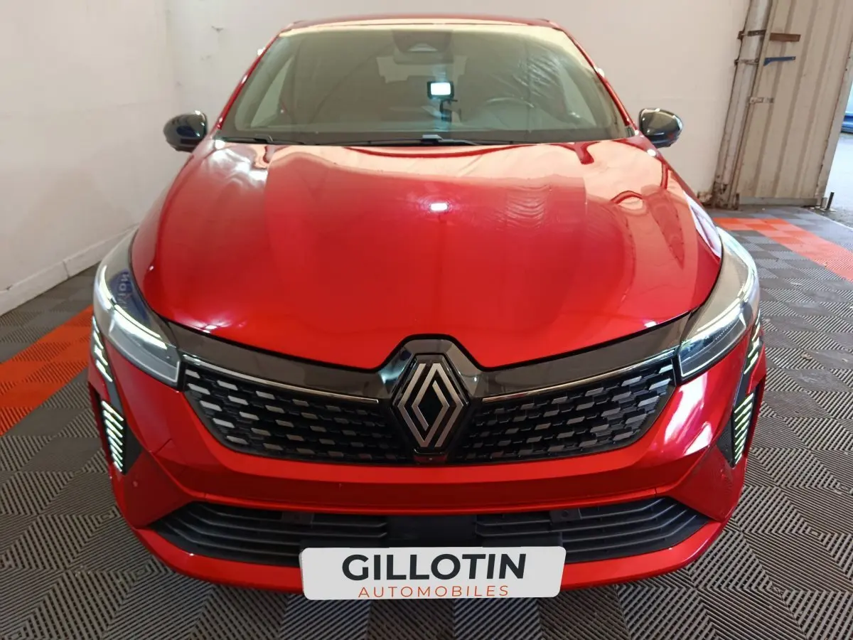 Vue avant d'une Renault Clio Techno TCe 90 rouge avec calandre noire et feux LED allumés dans un garage.