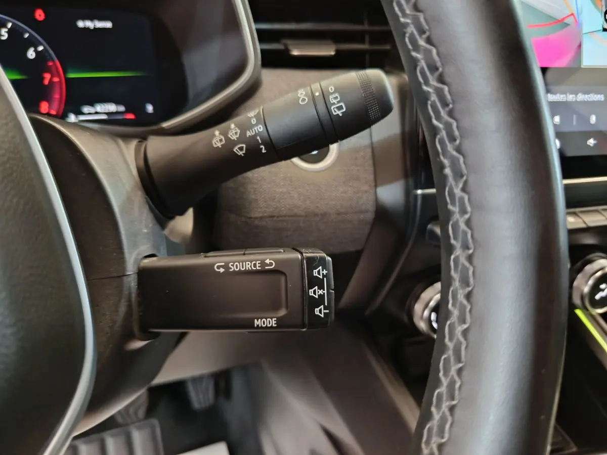 Gros plan sur la commande multifonctions à gauche du volant dans l’habitacle de la Renault Clio Techno TCe 90 rouge 2024.