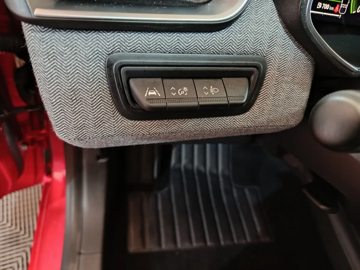 Détail des commandes d'assistance à la conduite sur tableau de bord gris, intérieur rouge visible côté conducteur Renault Clio 2024.