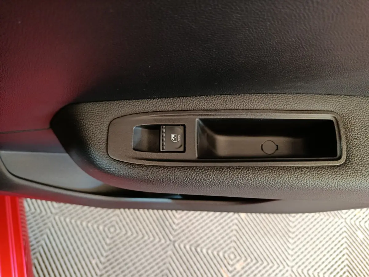 Gros plan sur le bouton de commande de la vitre électrique côté conducteur dans une Renault Clio rouge 2024.