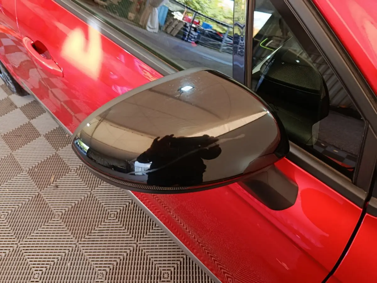 Rétroviseur noir en gros plan côté gauche d'une Renault Clio Techno TCe 90 rouge, vue partielle sur la porte.