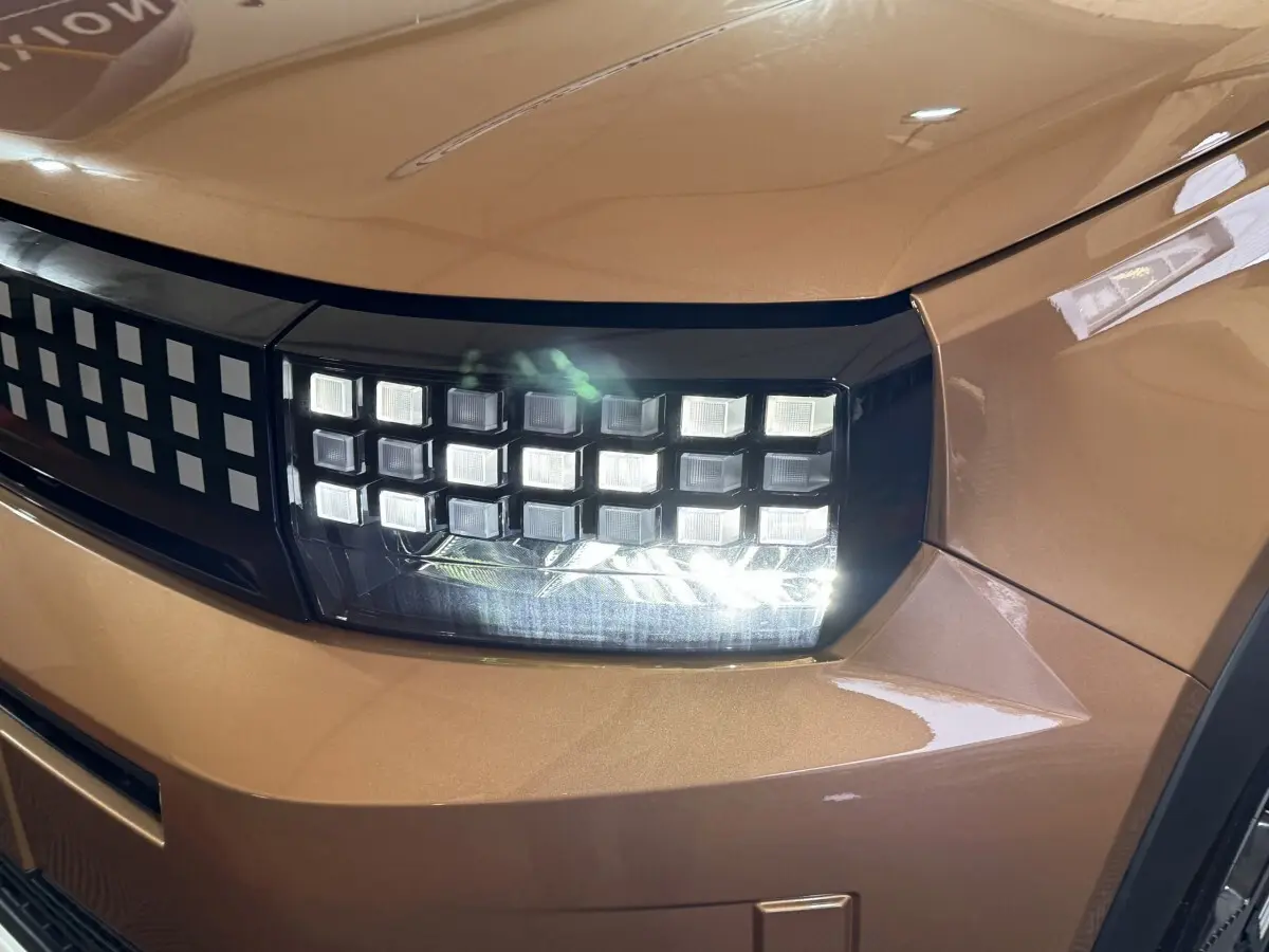 Gros plan sur le phare avant droit allumé de la FIAT Grande Panda marron avec calandre à motifs carrés.