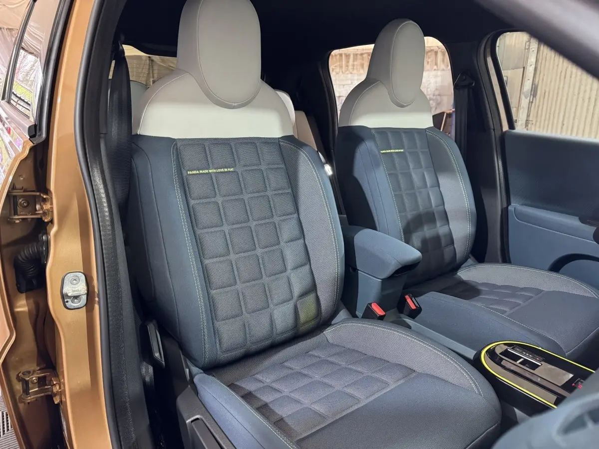 Vue intérieure des sièges avant bleu foncé et beige de la FIAT Grande Panda marron, porte ouverte côté gauche.