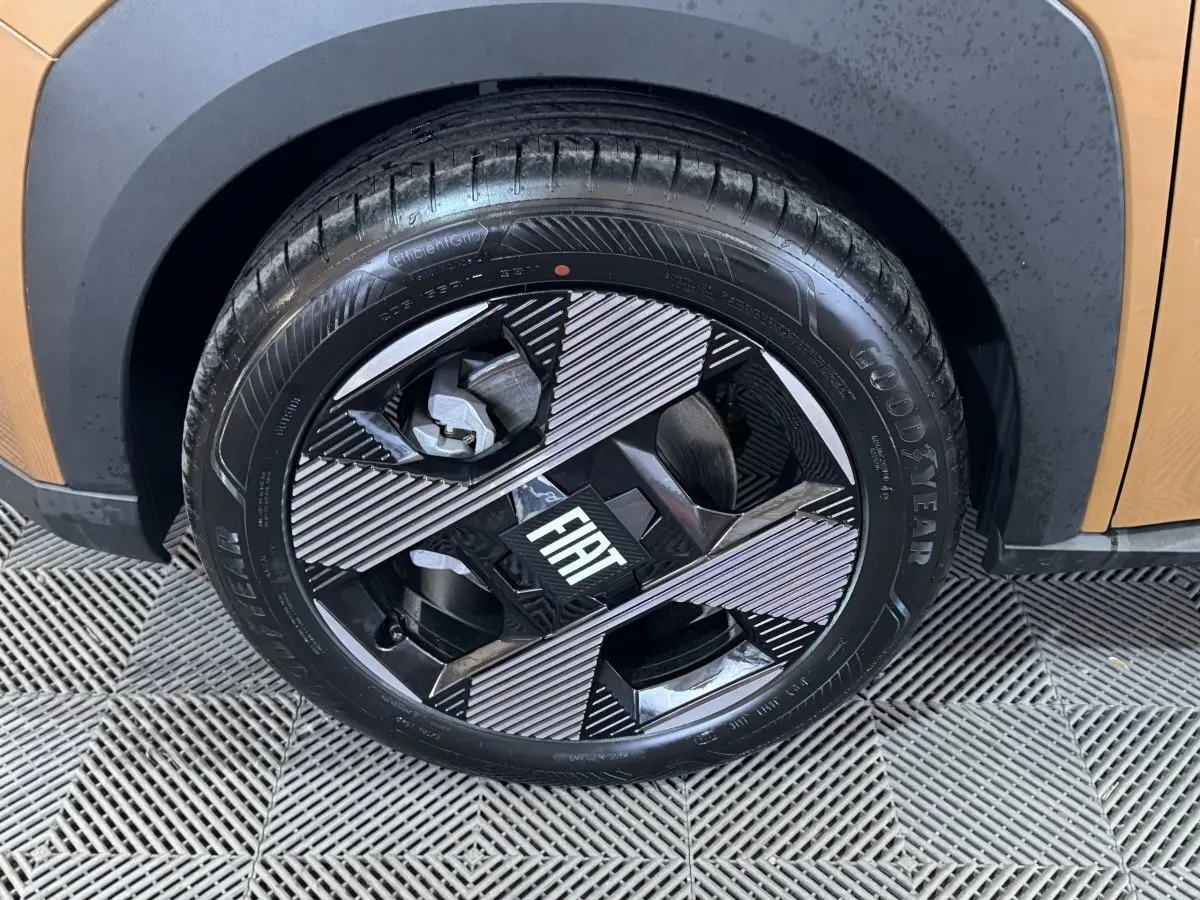 Gros plan sur la roue avant droite marron de la Fiat Grande Panda 1.2 Hybrid avec jante noire et argentée au design géométrique.