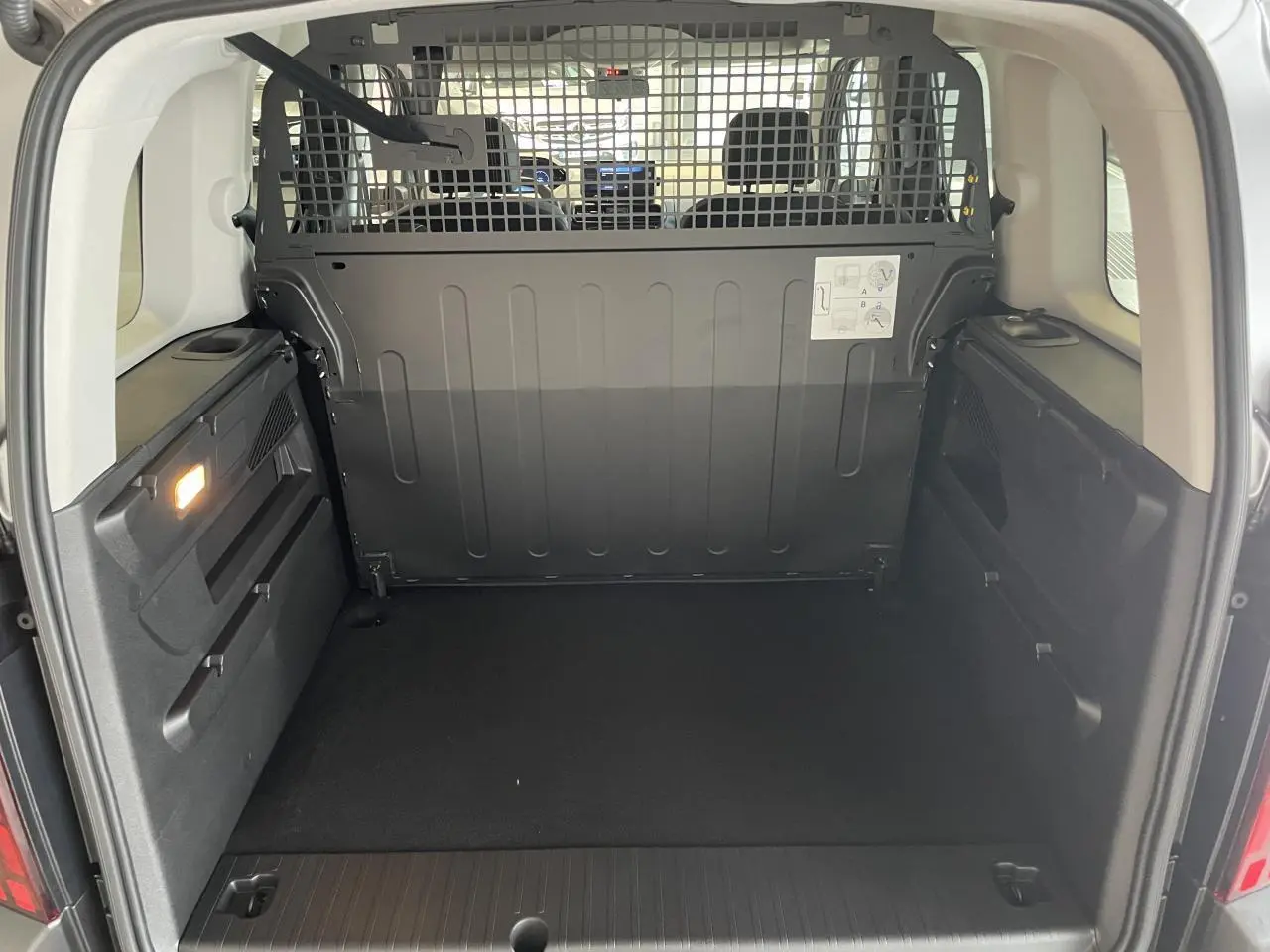 Vue arrière ouverte du Peugeot Rifter gris Artense, montrant l'espace de chargement avec cloison métallique de séparation.