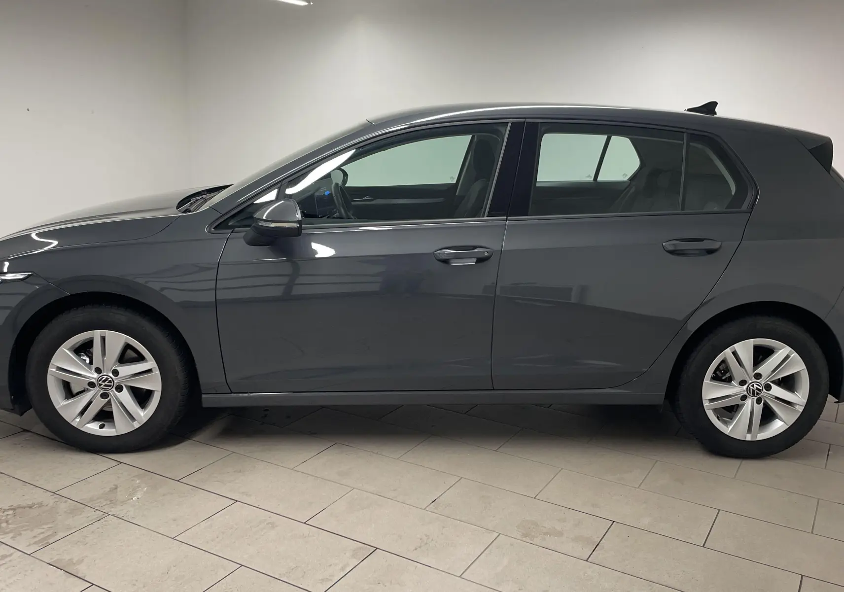 Profil côté gauche d'une Volkswagen Golf 1.5 TSI 116 BVM6 VW Edition gris dauphin métallisé, année 2024, en intérieur.