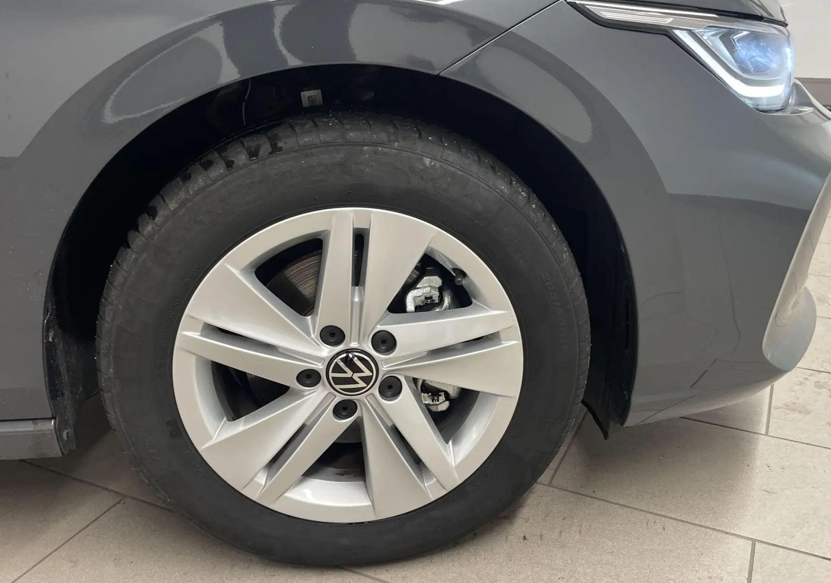 Gros plan sur la roue avant gauche et le phare d'une Volkswagen Golf 2024 gris dauphin métallisé.