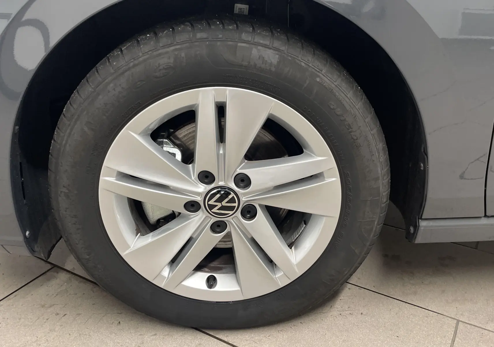 Gros plan sur la roue avant gauche d'une Volkswagen Golf 2024 Gris Dauphin avec jante alliage à 5 branches.