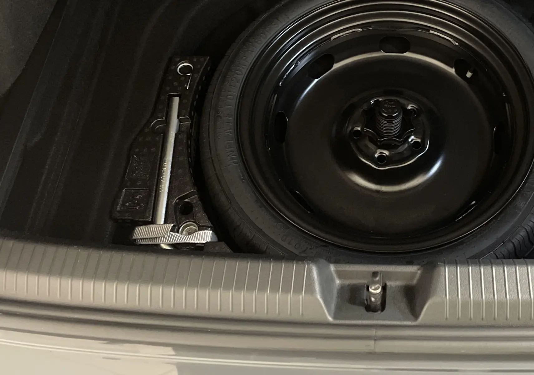 Gros plan sur la roue de secours noire et le cric dans le coffre d'une Volkswagen Golf Gris Dauphin 2024.