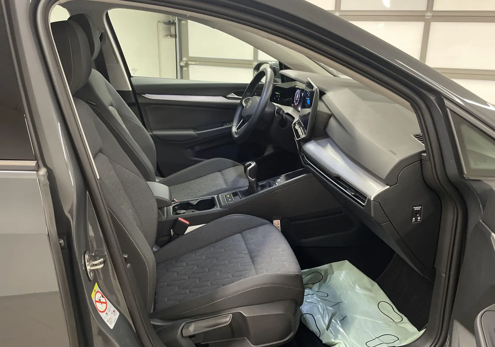 Intérieur avant droit de la Volkswagen Golf 1.5 TSI gris Dauphin, montrant sièges tissu et tableau de bord moderne.