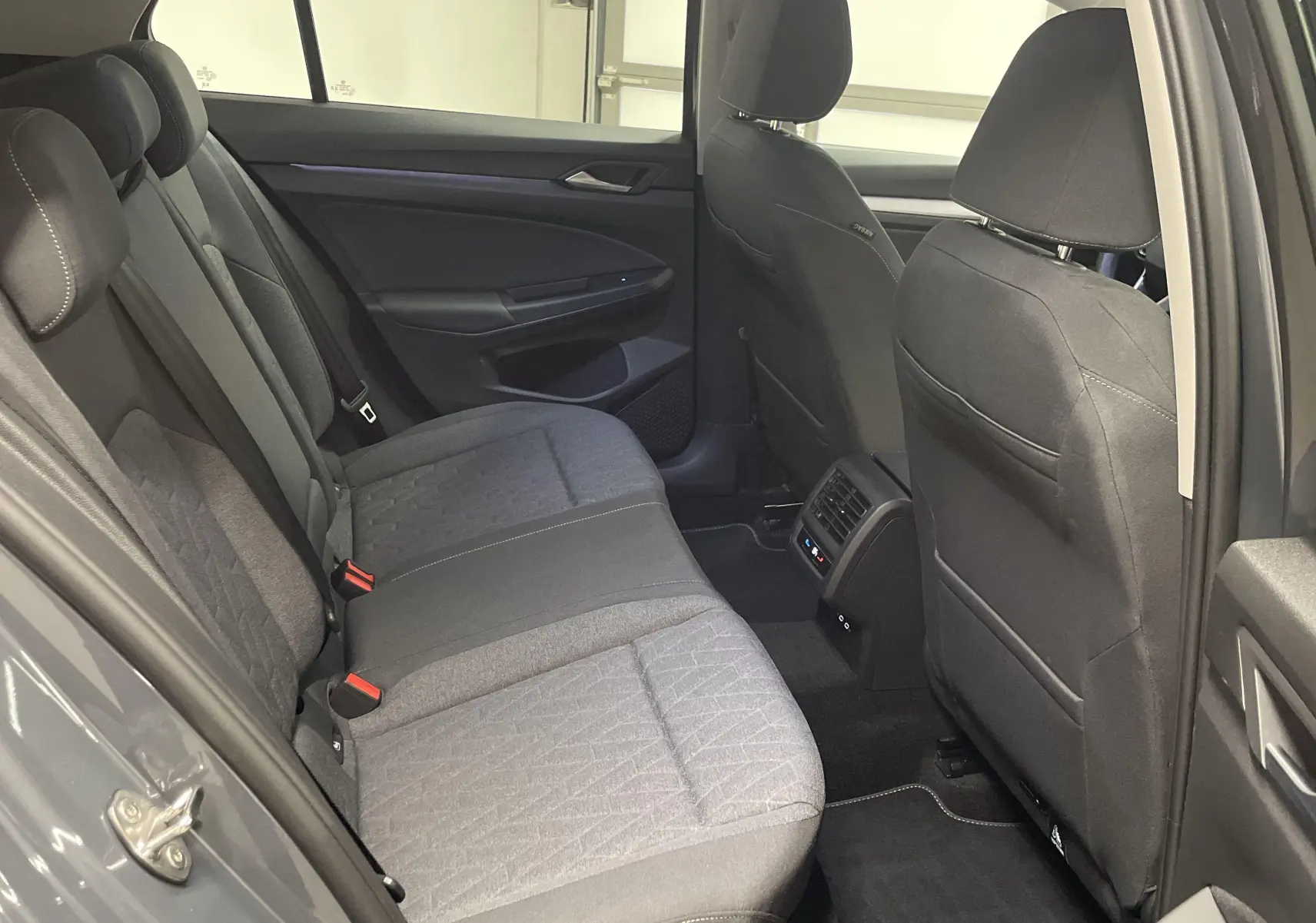 Vue intérieure arrière côté gauche de la Volkswagen Golf 1.5 TSI 2024 avec sièges tissu gris et aérations pour passagers arrière.