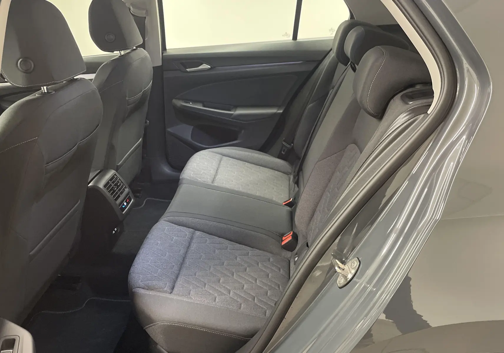 Intérieur arrière du Volkswagen Golf 2024 gris dauphin, sièges tissu gris avec motifs géométriques et aérateurs centraux.