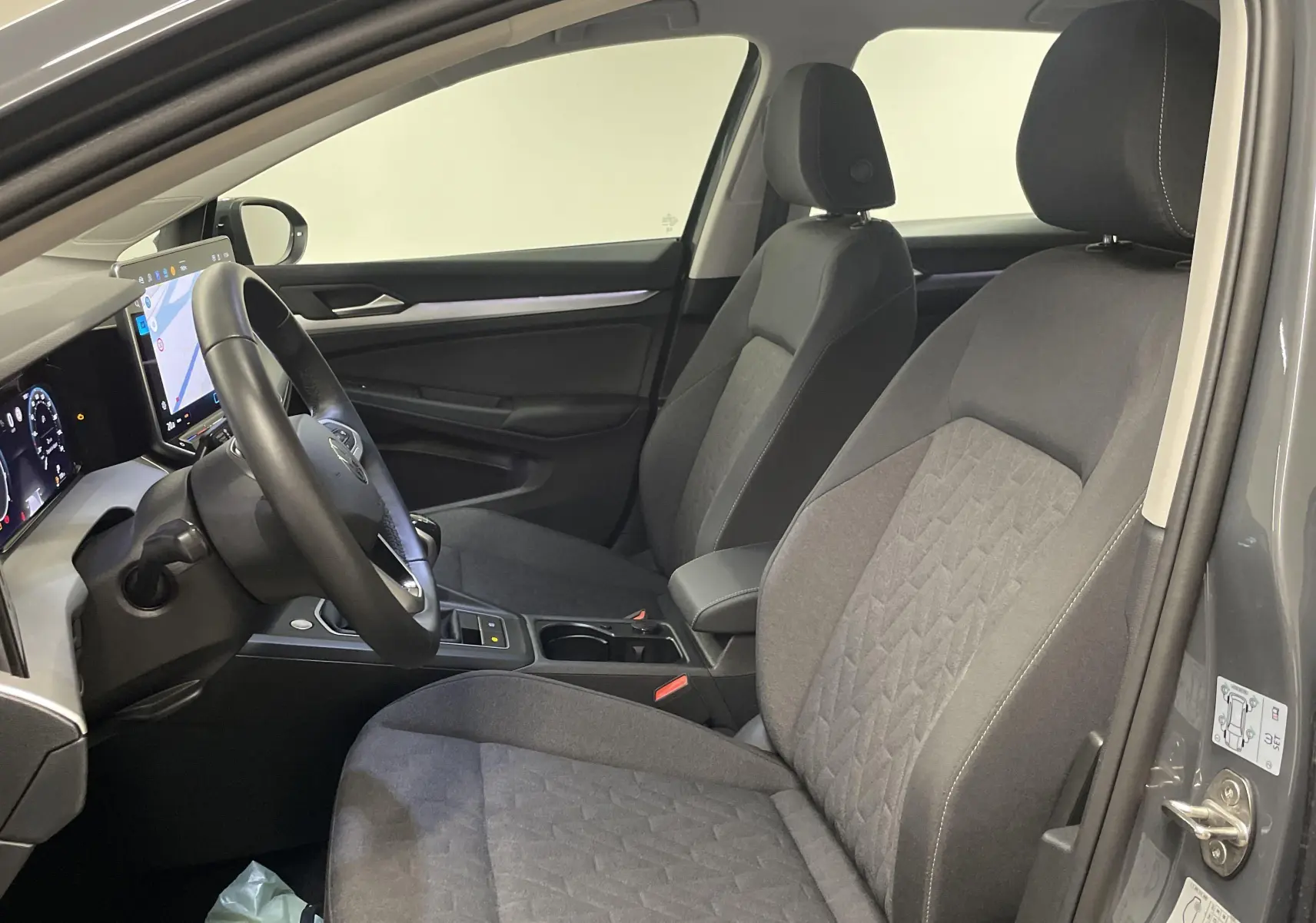 Intérieur avant de la Volkswagen Golf 1.5 TSI 2024 en Gris Dauphin, sièges tissu gris et tableau de bord numérique.