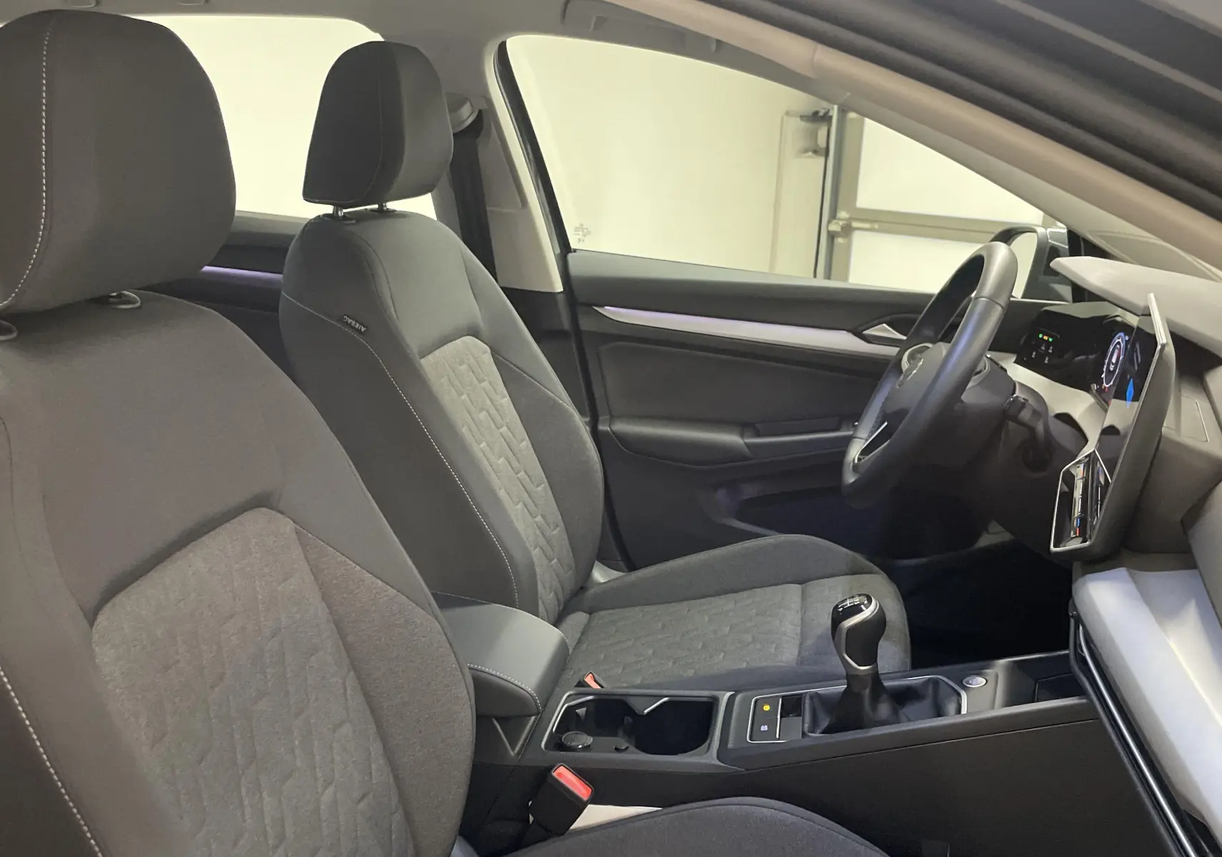 Intérieur avant de la Volkswagen Golf 1.5 TSI gris dauphin, sièges tissu gris et levier de vitesse manuel visible.