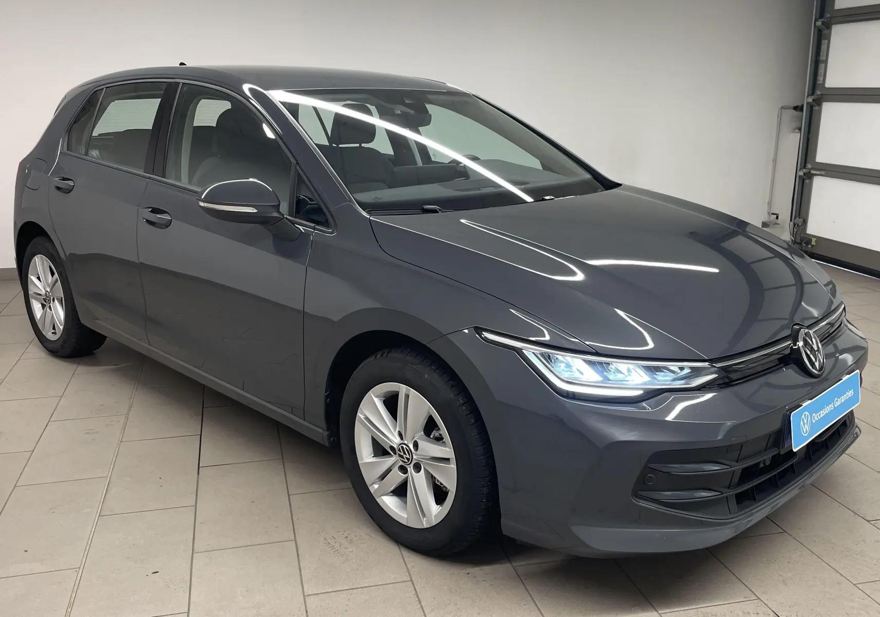Volkswagen Golf 1.5 TSI 2024 gris dauphin en 3/4 avant, phares allumés et jantes alliage visibles.