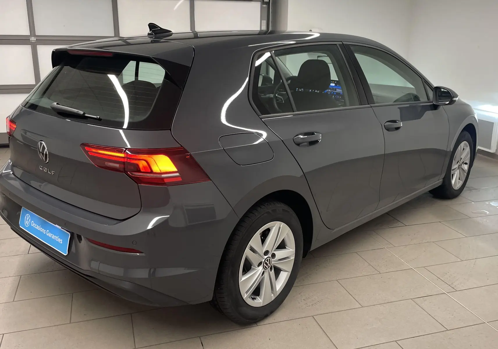 Volkswagen Golf 1.5 TSI gris dauphin vue 3/4 arrière droit en intérieur avec feux arrière allumés.