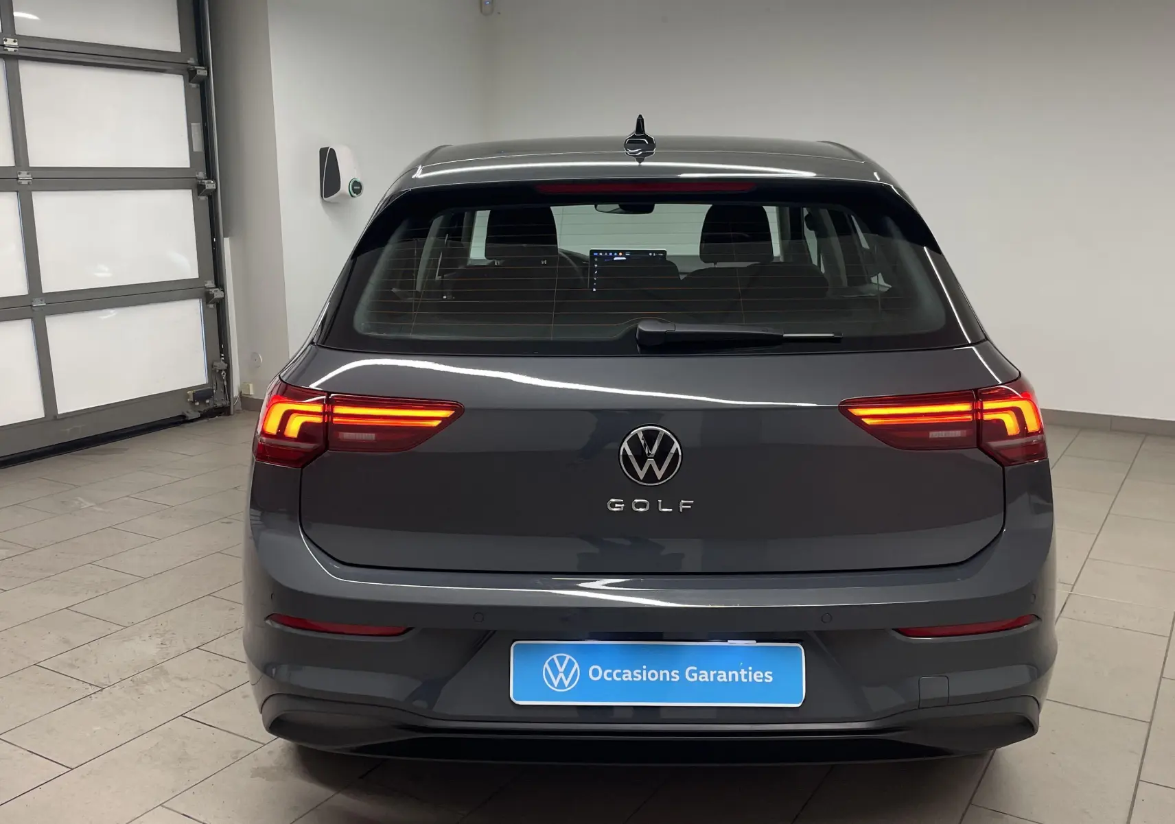 Vue arrière d'une Volkswagen Golf 1.5 TSI 116 Gris Dauphin avec feux allumés dans un garage lumineux.