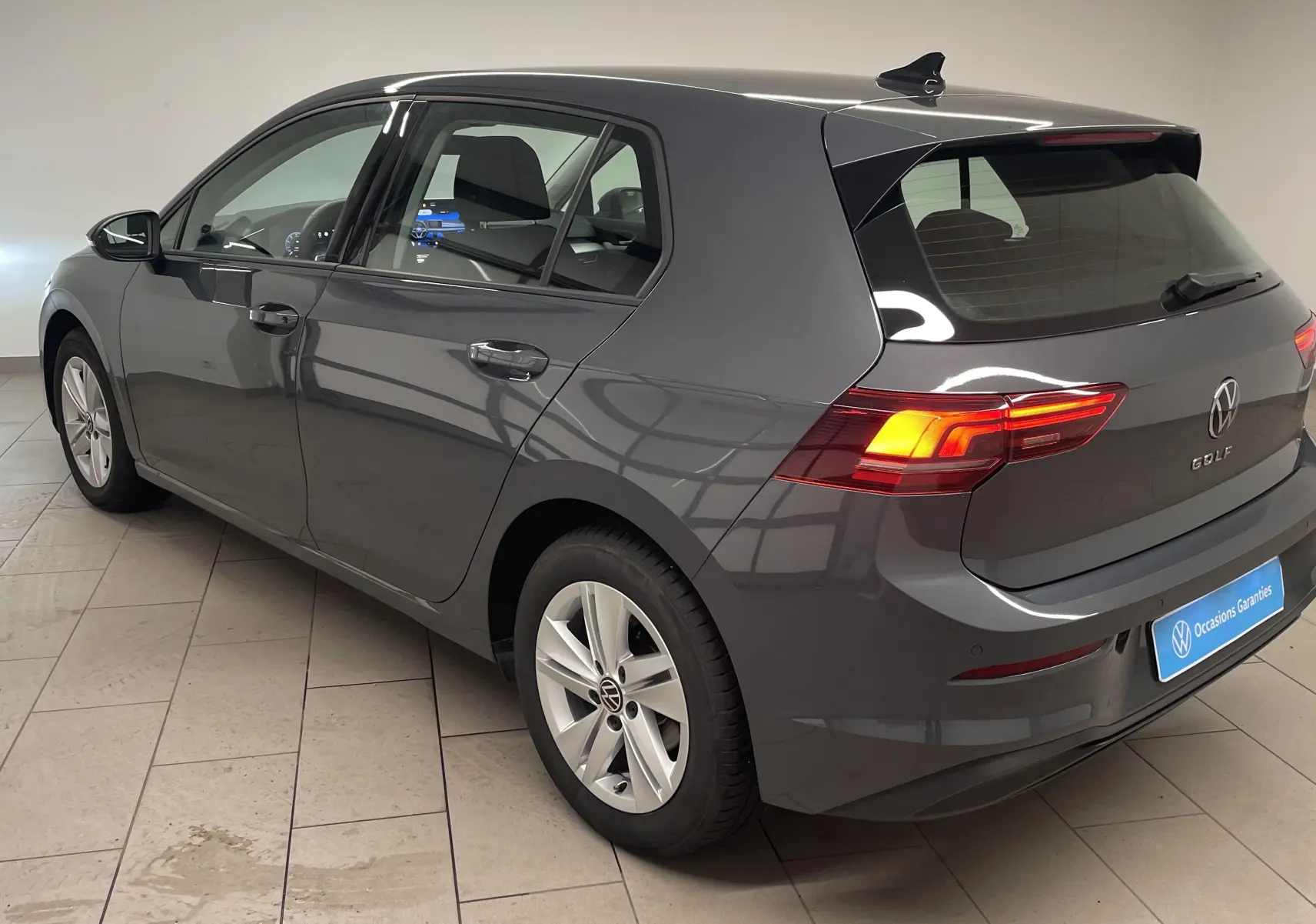 Volkswagen Golf 1.5 TSI gris dauphin vue 3/4 arrière droit en intérieur avec feux arrière allumés.