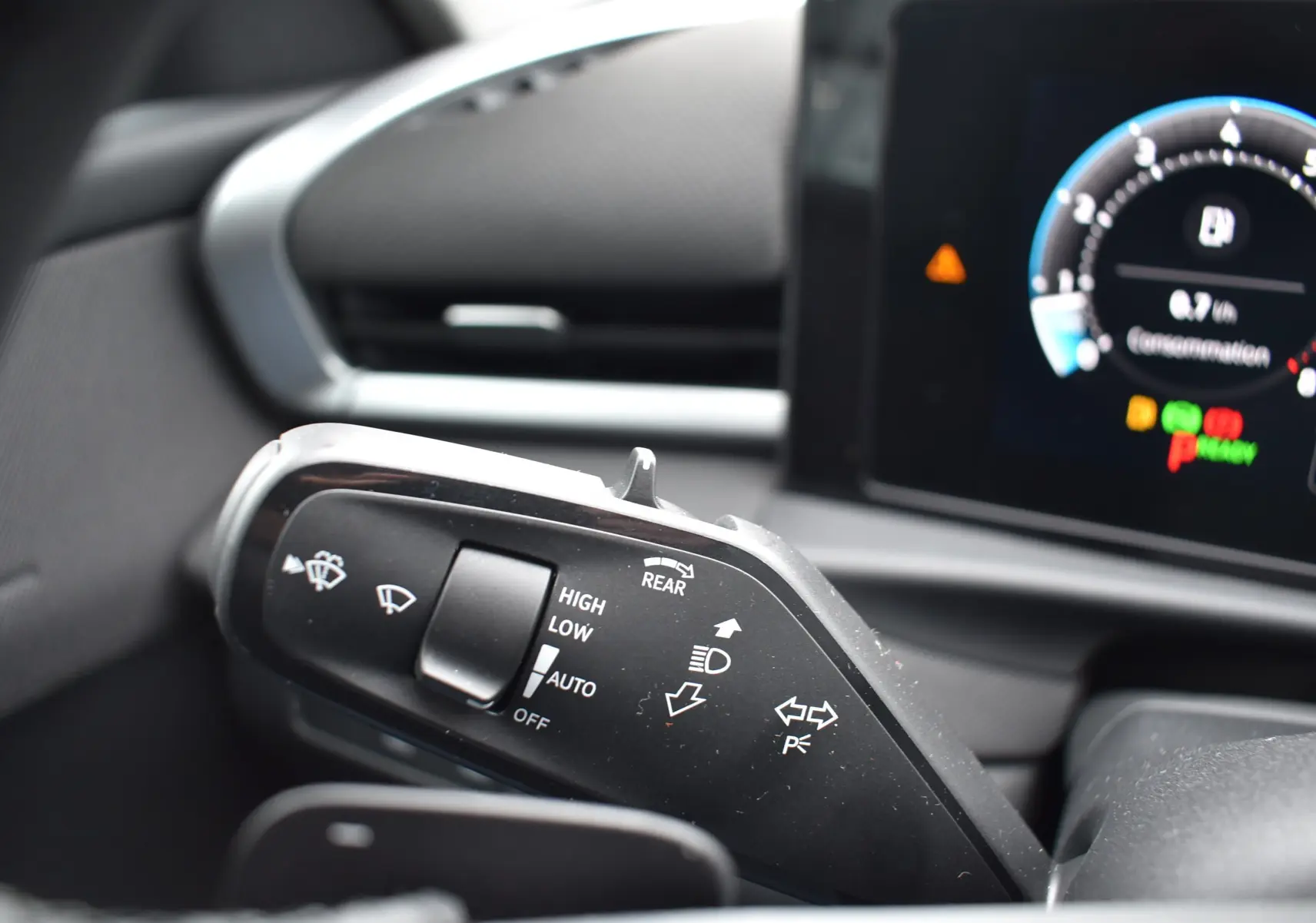 Gros plan sur la commande des essuie-glaces et clignotants dans l’habitacle du Volkswagen T-Roc blanc, tableau de bord numérique en arrière-plan.