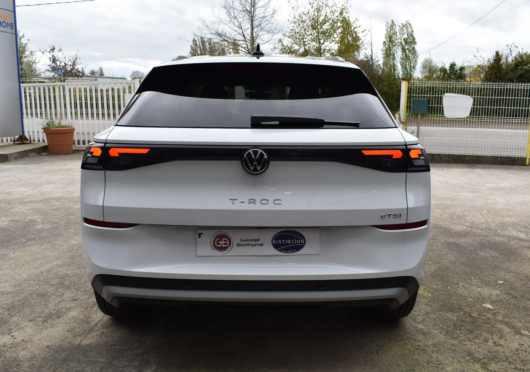 Vue arrière d'un Volkswagen T-Roc blanc 2025 avec feux LED allumés et logo central visible.