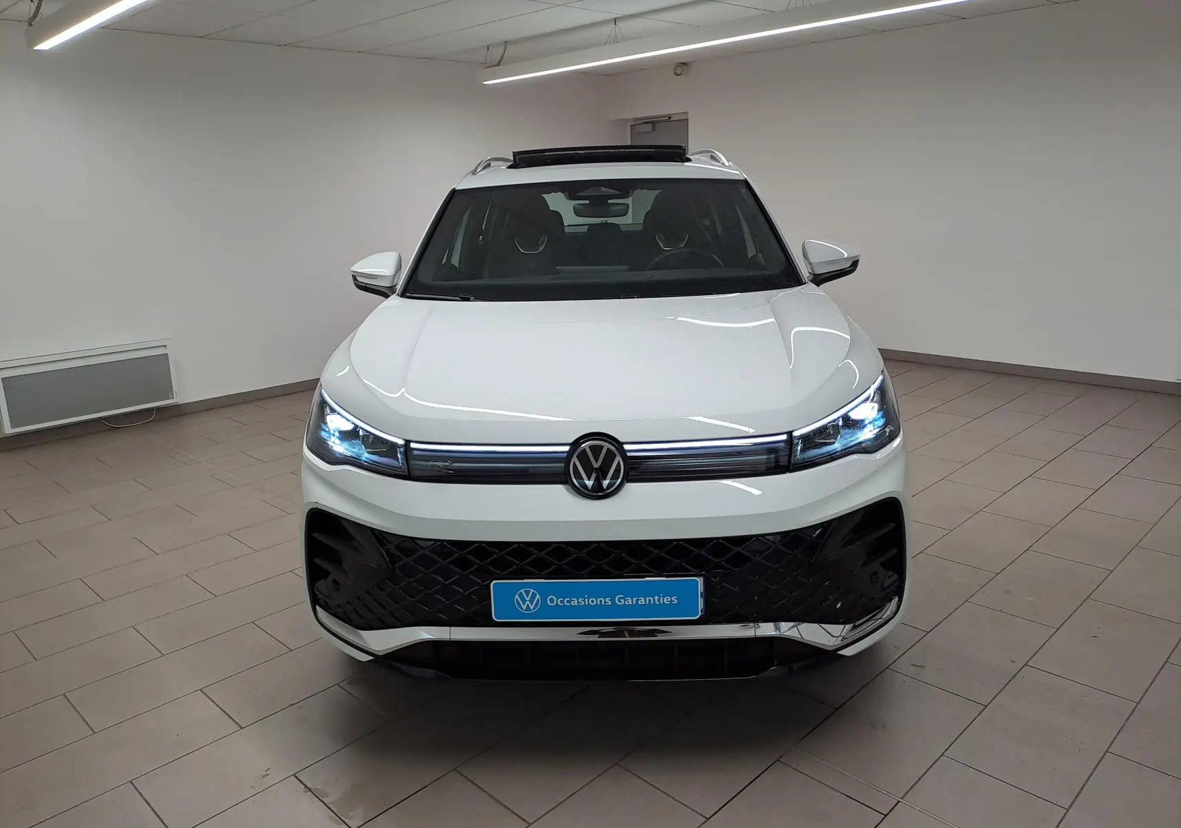 Vue avant d'un Volkswagen Tiguan blanc pur avec phares LED allumés et calandre R-Line dans un showroom.