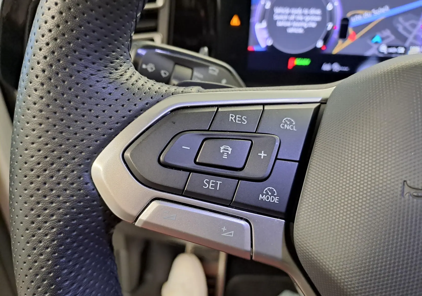 Gros plan sur les commandes du volant côté gauche du Volkswagen Tiguan blanc, avec boutons de régulateur de vitesse et assistance conduite.