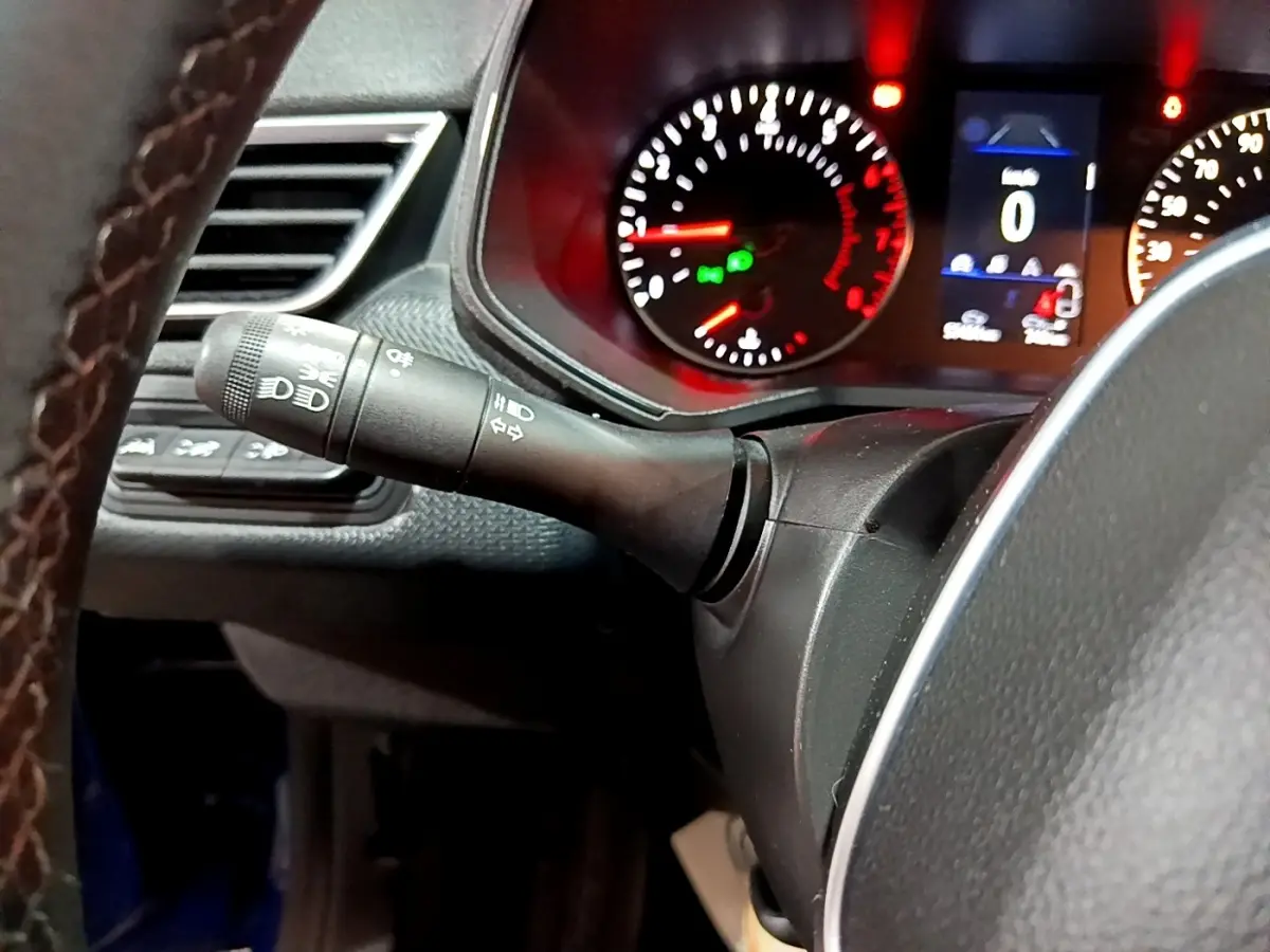 Gros plan sur le commodo des phares à gauche du volant cuir, avec tableau de bord éclairé en rouge de la Renault Clio Business.