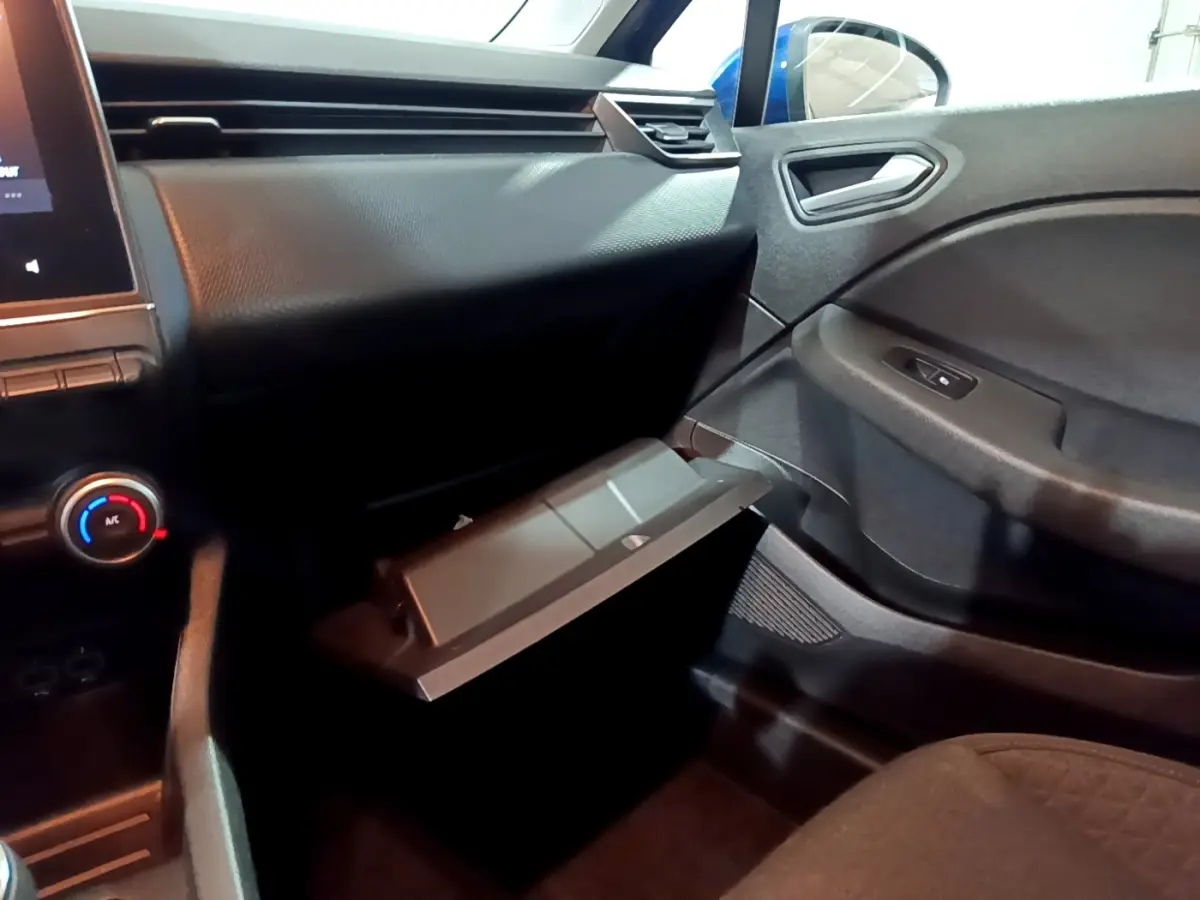 Intérieur de la Renault Clio Business bleu, vue côté passager avec boîte à gants ouverte et tableau de bord noir.